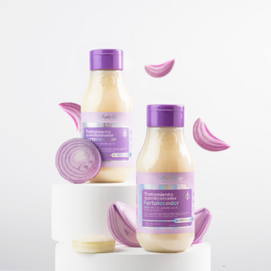 Dos botellas de tratamiento capilar fortalecedor de 550 ml con extracto de cebolla y ajo, decoradas con rodajas de cebolla morada sobre soportes blancos.